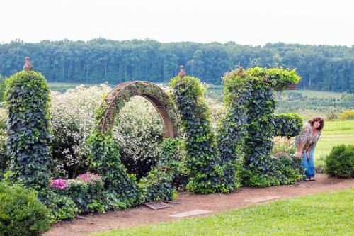 A person poses next to a large, green "LOVE" sign made of vines and flowers in a scenic garden.