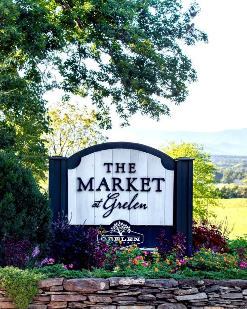 Sign for "The Market at Grelen" surrounded by greenery and colorful flowers, with mountains in the background.
