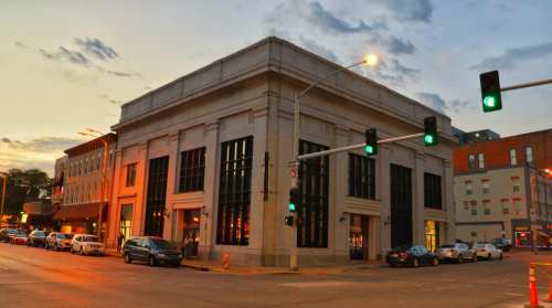 Historic building at sunset, with traffic lights and parked cars in a bustling urban setting.