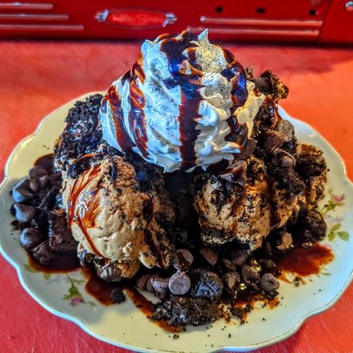 A decadent dessert featuring ice cream topped with whipped cream, chocolate sauce, cookie crumbles, and chocolate chips.