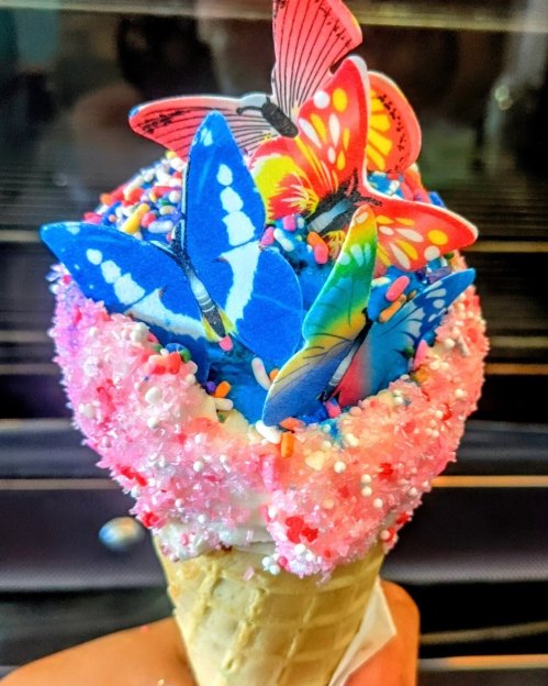 A colorful ice cream cone topped with pink sprinkles and decorative butterfly cutouts.