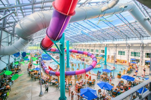 A vibrant indoor water park with colorful slides, a pool, and people enjoying the space under a glass roof.