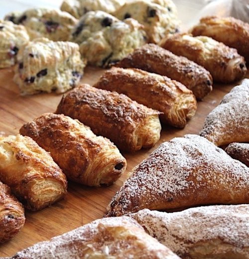A variety of freshly baked pastries, including croissants and scones, arranged on a wooden board.