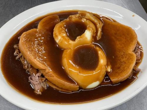 A plate of pulled pork topped with two slices of bread, gravy, and a side of mashed potatoes.