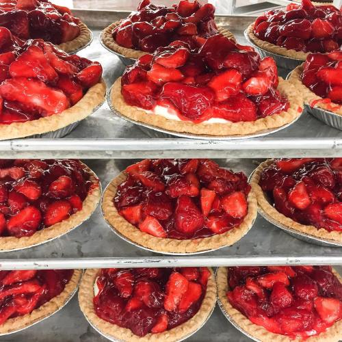 Freshly baked strawberry pies with a glossy red glaze, arranged on a shelf.
