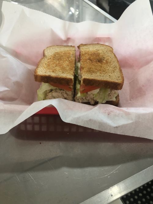 A toasted sandwich with lettuce and tomato, cut in half, served in a red basket lined with white paper.