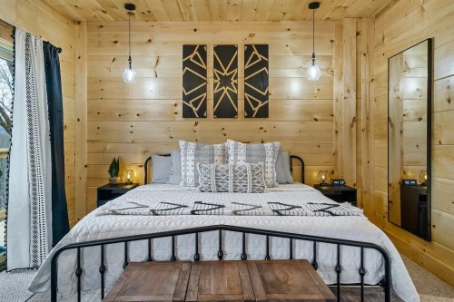 Cozy bedroom with wooden walls, a bed with decorative pillows, and stylish lighting fixtures.