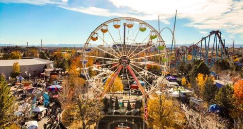 Aerial view of a vibrant amusement park featuring a large Ferris wheel and roller coasters, surrounded by autumn trees.