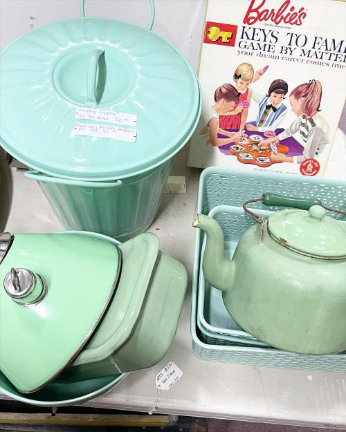 A collection of mint green kitchen items, including a trash can, pots, and a kettle, alongside a Barbie game box.