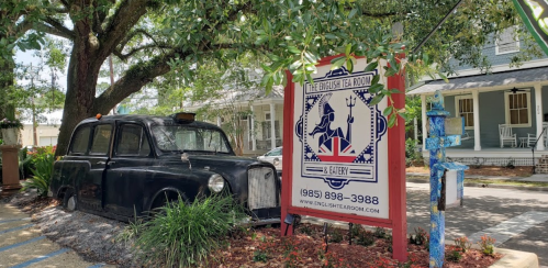 A vintage black taxi cab parked beside a colorful sign for "The English Tea Room" under a tree.