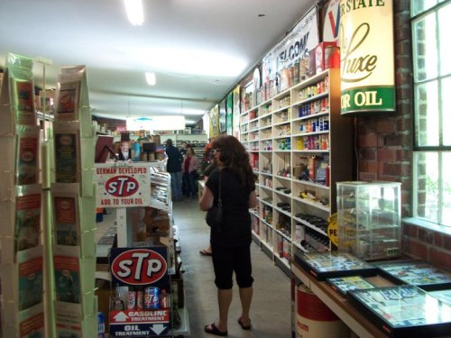 A vintage store interior with shelves of oil products and memorabilia, and a person browsing the aisles.