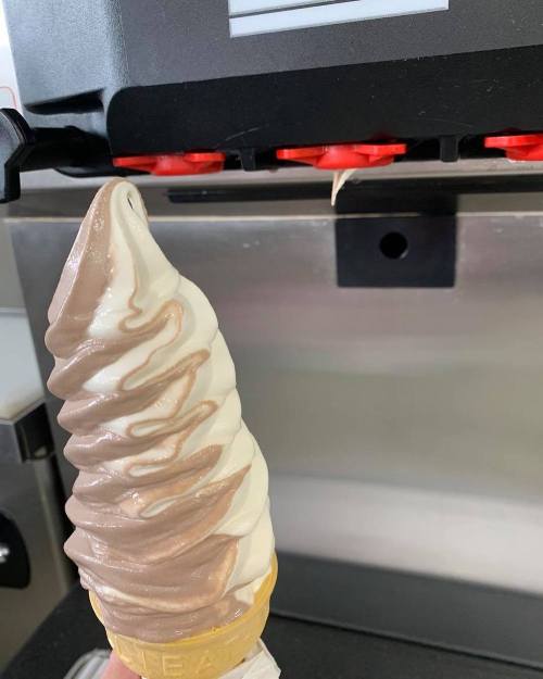 A soft-serve ice cream cone with chocolate and vanilla swirls, held under a dispensing machine.