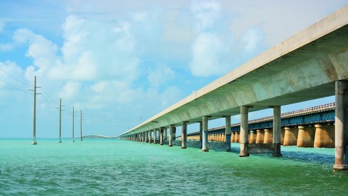 A long concrete bridge stretches over turquoise waters under a blue sky with scattered clouds.