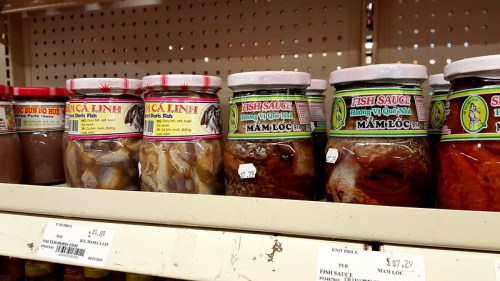 Jars of fish sauce on a store shelf, labeled in Vietnamese, with prices visible.