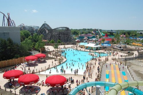A vibrant amusement park scene with a large pool, water slides, and crowds enjoying the sunny day.