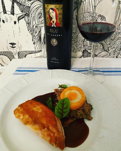 A plate of salmon with sauce, garnished with vegetables, alongside a bottle of red wine and a glass.