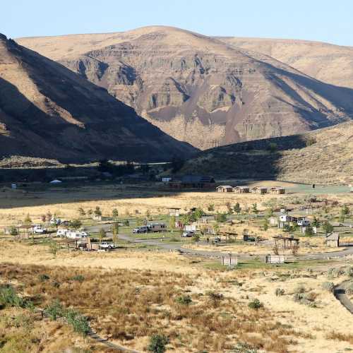 A scenic view of a valley surrounded by mountains, featuring a small settlement and dry, grassy terrain.