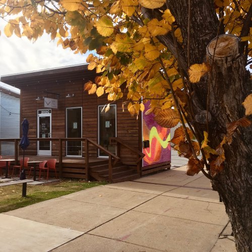 A small wooden building with a colorful mural, surrounded by autumn leaves and outdoor seating.