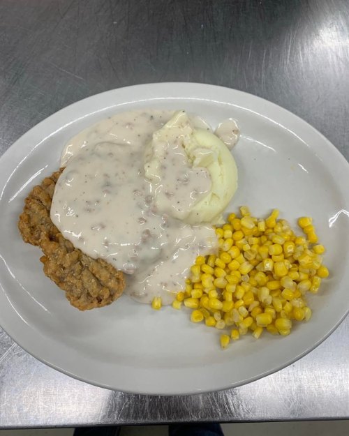A plate of mashed potatoes topped with gravy, two sausage patties, and a side of corn.
