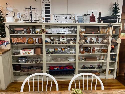 A display shelf filled with various vintage items, including kitchenware, decor, and collectibles in a cozy setting.