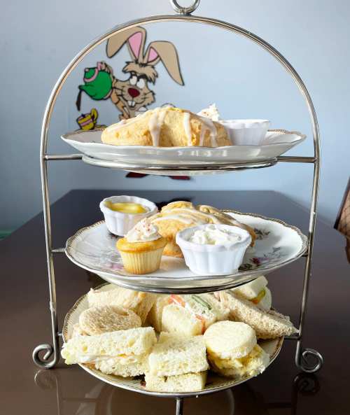 A tiered stand with assorted sandwiches, pastries, and small desserts, set against a colorful cartoon backdrop.