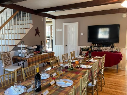A dining room set for a gathering, featuring a long table with place settings, a buffet, and a TV on the wall.