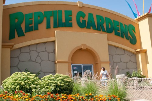 A colorful entrance to Reptile Gardens, featuring large green signage and vibrant flower beds in front.