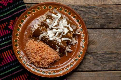 A plate of enchiladas topped with onions and sesame seeds, served with a side of orange rice on a wooden table.