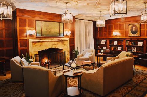 Cozy living room with a fireplace, elegant seating, wooden paneling, and bookshelves filled with books. Warm ambiance.