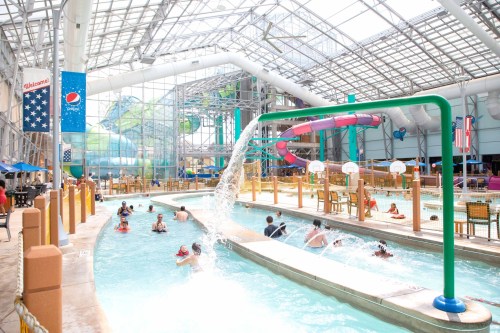 Indoor water park featuring a lazy river, water slides, and families enjoying the attractions under a glass roof.