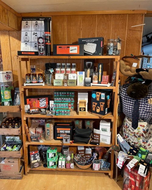 A wooden shelf filled with various novelty gifts, kitchen items, and accessories in a cozy store setting.