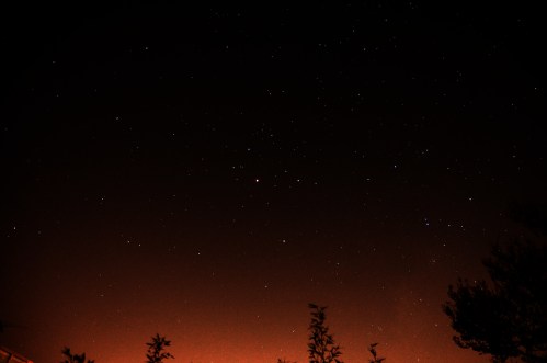 A starry night sky with scattered stars against a dark backdrop, illuminated by a faint orange glow at the horizon.