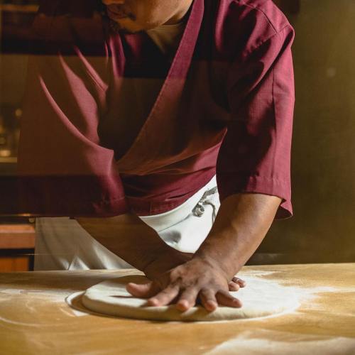 A chef in a red shirt kneads dough on a floured surface, focused on preparing a dish.