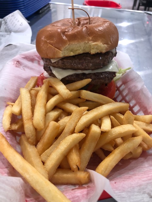 A double cheeseburger with lettuce and tomato, served with a side of golden French fries in a red basket.