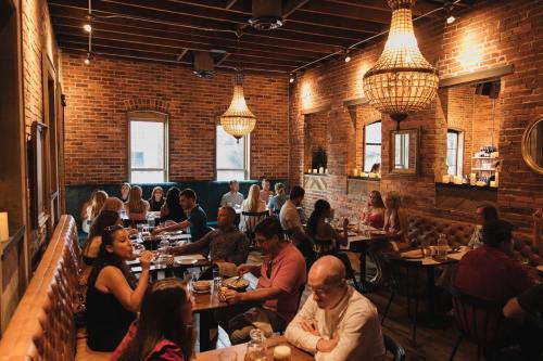 A lively restaurant interior with brick walls, chandeliers, and diners enjoying meals and drinks at various tables.
