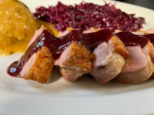 A plate featuring sliced duck breast with berry sauce, red cabbage, and a side of mashed squash.