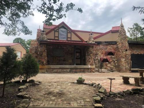 A rustic stone house with a red roof, surrounded by greenery and a stone pathway.