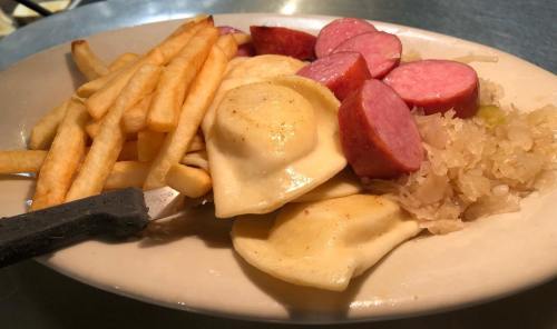 A plate of pierogi, sausage slices, sauerkraut, and French fries.