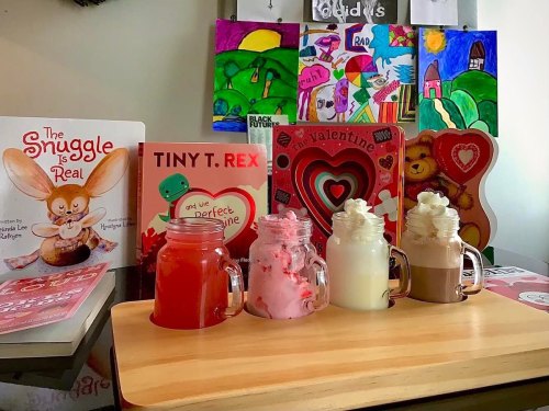 A colorful display of books and Valentine's decorations with four jars of drinks topped with whipped cream.