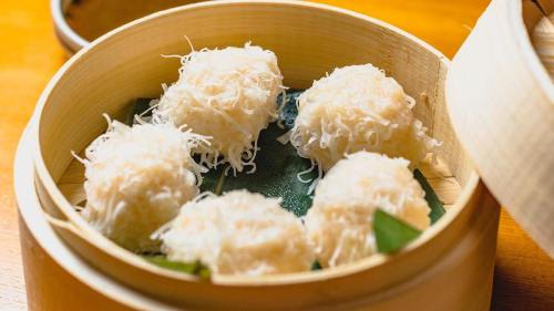 A bamboo steamer filled with six fluffy, white dumplings topped with fine, shredded coconut.