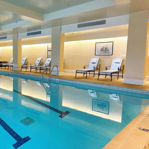 Indoor swimming pool with lounge chairs and soft lighting, reflecting on the water's surface.