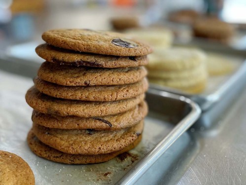 A stack of freshly baked cookies on a baking tray, with more cookies in the background.