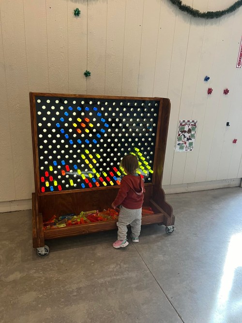 A toddler interacts with a colorful light board, creating patterns with illuminated pegs in a playful indoor setting.
