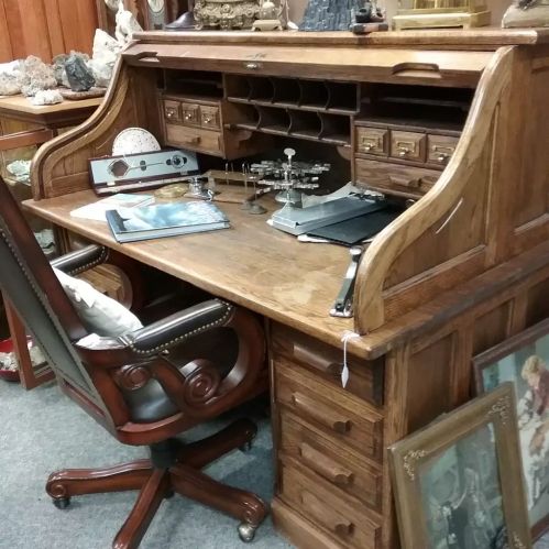 A vintage wooden desk with a chair, featuring various decorative items and an organized workspace.