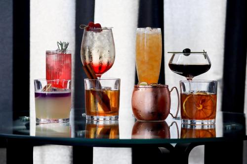 A variety of colorful cocktails displayed on a glass table, featuring garnishes and unique glassware.