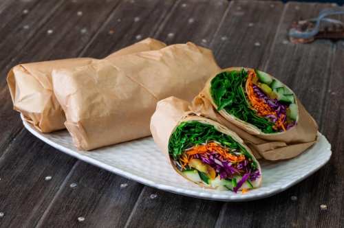 A plate with two wrapped veggie wraps and one cut in half, showcasing colorful vegetables inside.