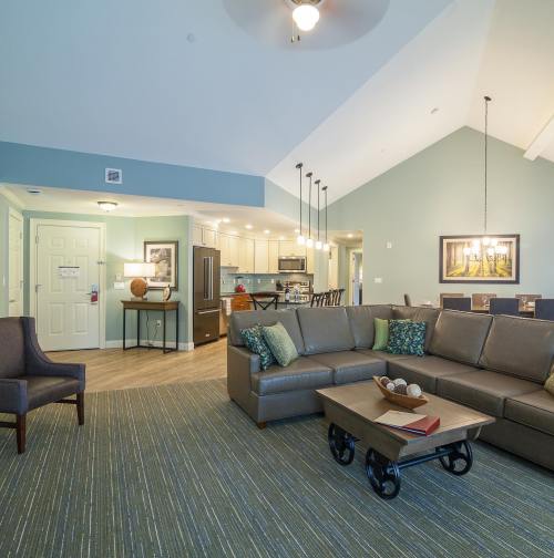 A spacious living area with a sofa, armchair, and dining table, featuring modern decor and a kitchen in the background.