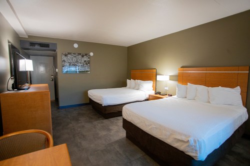A hotel room featuring two beds, a desk, a TV, and modern decor in neutral tones.