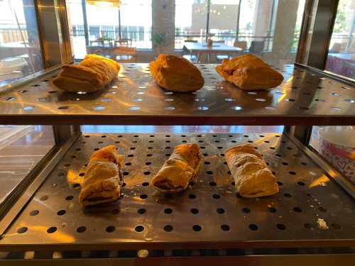 A display case with freshly baked pastries, including croissants and chocolate-filled rolls, on metal trays.