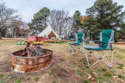 A campsite with a fire pit, two folding chairs, and a tent in a wooded area.